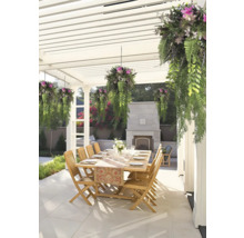Eethoek buiten onder een witte pergola met houten tafel, houten stoelen, hangplanten en een stenen open haard op een betegeld terras.