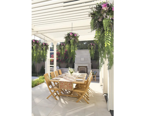 Eethoek buiten onder een witte pergola met houten tafel, houten stoelen, hangplanten en een stenen open haard op een betegeld terras.