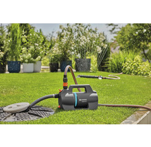 Gardena tuinpomp 5000 Silent op een gazon in een lichte tuin met aangesloten slang en sproeier voor irrigatie.
