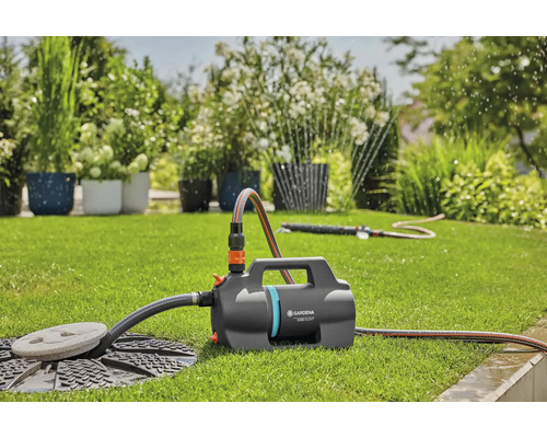 Gardena tuinpomp 5000 Silent op een gazon in een lichte tuin met aangesloten slang en sproeier voor irrigatie.