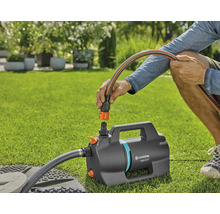 Persoon sluit een tuinslang aan op de Gardena tuinpomp 5000 Silent op een gazon.