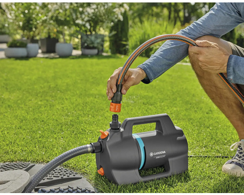 Persoon sluit een tuinslang aan op de Gardena tuinpomp 5000 Silent op een gazon.
