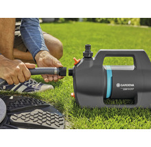 Een Gardena tuinpomp 5000 Silent wordt op een gazon aangesloten op een grijze tuinslang.