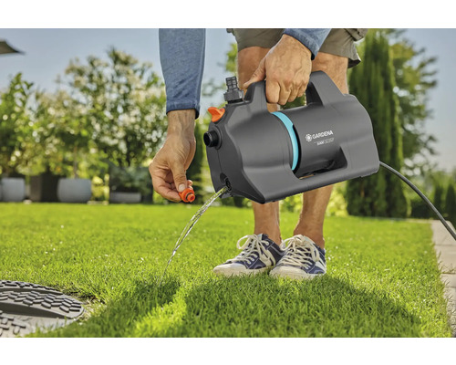 Persoon leegt een Gardena besproeiingspomp 5500 Silent op een gazon in de tuin.