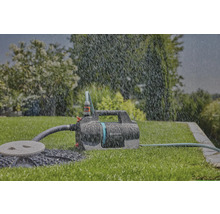 Gardena tuinpomp op een gazon in de regen met aangesloten tuinslangen.