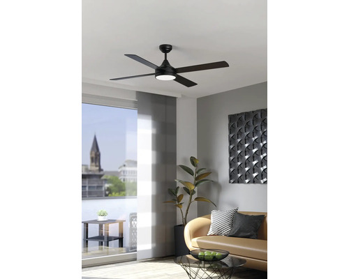 Moderne zwarte plafondventilator met vijf bladen en geïntegreerde lamp in een lichte woonkamer met bank en kamerplant.