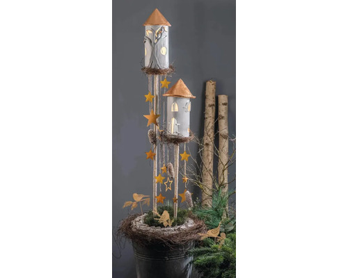 Decoratieve torens met verlichte ramen, hangende sterren en dennenappels in een rustieke nestbasis met groen en vogels.