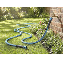 Textiele tuinslang aangesloten op een buitenkraan aan een bakstenen muur, liggend op een gazon in de tuin.