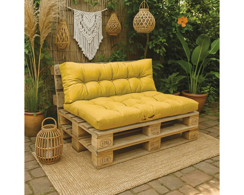 Palletbank met gele kussens gemaakt van Europallets in een gezellige tuin met boho-decoratie, planten en rieten windlichten.