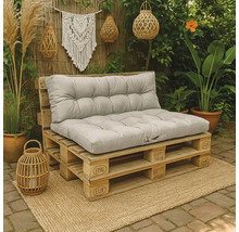 Palletbank van Europallets met grijze gecapitonneerde kussens in een tuin op een jute mat naast planten en decoratie.