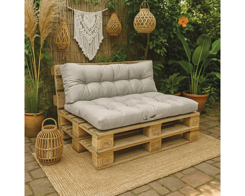 Palletbank van Europallets met grijze gecapitonneerde kussens in een tuin op een jute mat naast planten en decoratie.