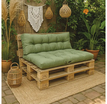 Palletbank voor buiten met groene kussens op een jute kleed, omgeven door planten en boho decoratie zoals lantaarns.