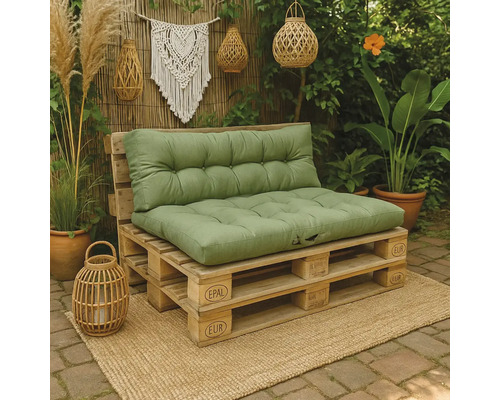 Palletbank voor buiten met groene kussens op een jute kleed, omgeven door planten en boho decoratie zoals lantaarns.