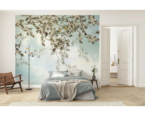 Lichte slaapkamer met fotobehang van bloeiende takken en vogels, bed, houten loungestoel met leer en visgraatvloer.