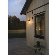 Buitenwandlamp op een houten gevel naast een raam bij schemering, houten terras met een bijzettafel.