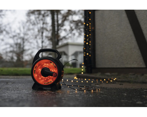 LED-lichtsnoer op een zwarte haspel voor buiten met warmwit licht op een natte ondergrond naast een gebouw.