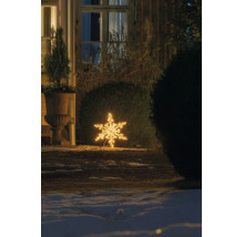 Warmwitte LED-sneeuwvlok als buitenverlichting, geplaatst op de grond in een winterse tuin 's nachts bij een struik en een huis.