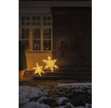 Twee verlichte LED-sneeuwvlokken in verschillende maten als kerstdecoratie voor een huisingang op stenen treden met warmwit licht.