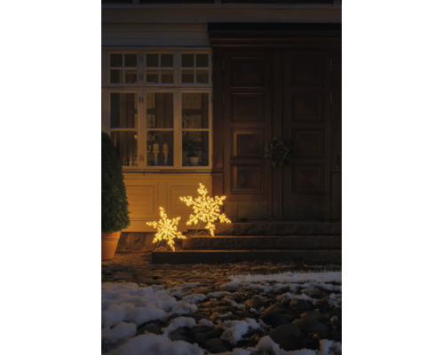 Twee verlichte LED-sneeuwvlokken in verschillende maten als kerstdecoratie voor een huisingang op stenen treden met warmwit licht.