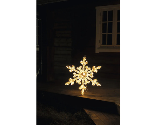 Verlichte LED-sneeuwvlok met warm wit licht als kerstdecoratie op een houten terras voor een huis bij nacht.