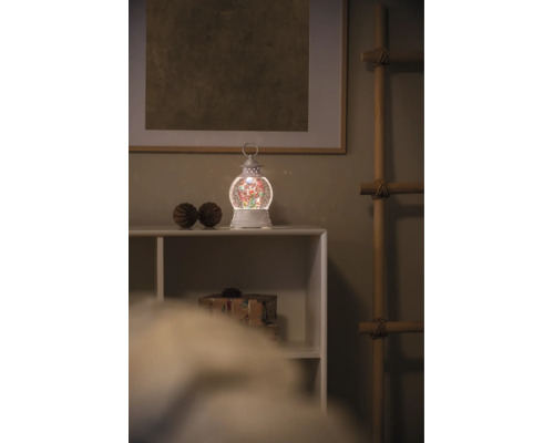 Kerst waterlantaarn met LED-verlichting en glitters op een witte plank in een kerstomgeving.