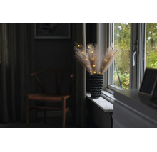 Kunstmatig pampasgras met LED-verlichting in een vaas met textuur op een vensterbank.