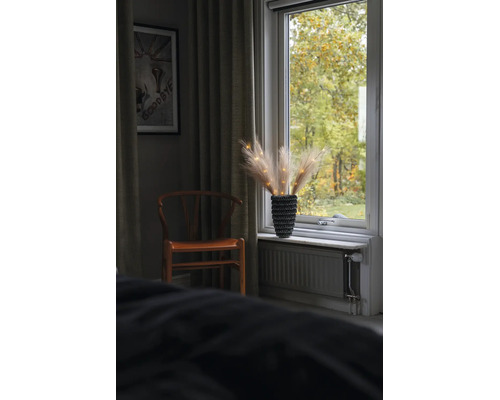 Kamerinterieur met houten stoel en vensterbankdecoratie van pampasgras in een getextureerde vaas met lichtjes.