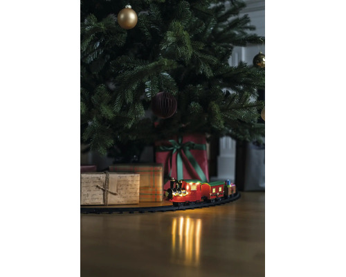 Kersttrein op rails onder een versierde kerstboom met cadeaus op een houten vloer.