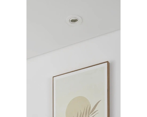 Witte inbouwspot in een licht plafond boven een minimalistisch schilderij aan een witte muur.