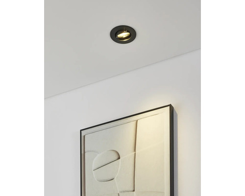 Inbouwspot in het plafond verlicht een ingelijst kunstwerk met textuur aan een muur.