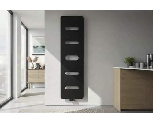 Moderne verticale designradiator in zwart met horizontale uitsparingen aan een witte muur in een lichte minimalistische kamer.