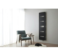 Zwarte designradiator aan een grijze muur in een lichte woonkamer met fauteuil, bijzettafel en wit tapijt.