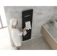Moderne zwarte designradiator aan een marmeren wand in de badkamer met een persoon in een witte badjas en handdoeken.
