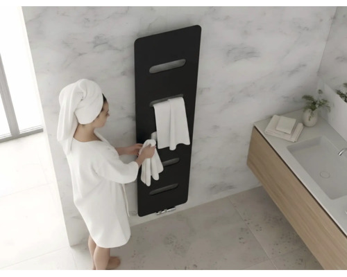 Moderne zwarte designradiator aan een marmeren wand in de badkamer met een persoon in een witte badjas en handdoeken.