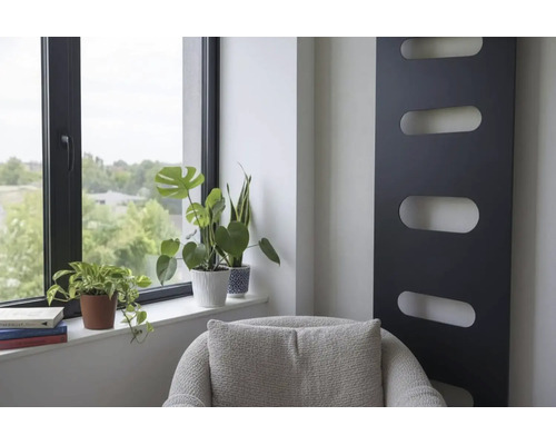 Modern interieur met zwarte verticale designradiator, kamerplanten bij het raam en grijze fauteuil.