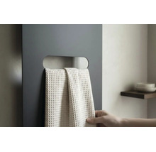 Donkergrijze vlakke radiator met horizontale uitsparing als handdoekhouder en een lichte handdoek met wafelstructuur.