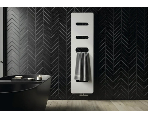 Moderne witte paneelradiator aan een zwart betegelde wand in visgraatmotief in een badkamer met een donker ligbad.