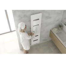 Moderne witte handdoekradiator in een lichte badkamer met marmerlook en een persoon in een badjas.