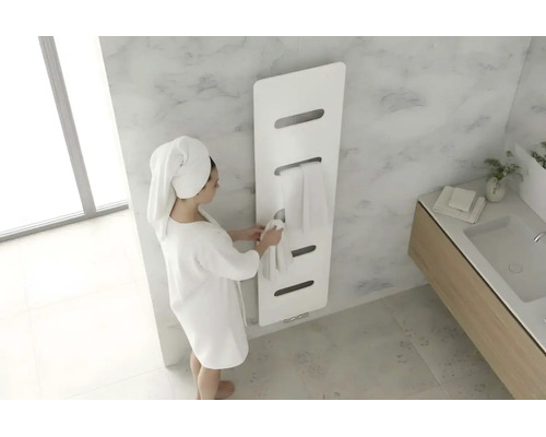 Moderne witte handdoekradiator in een lichte badkamer met marmerlook en een persoon in een badjas.