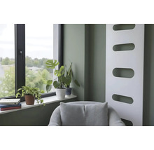 Moderne woonkamer met saliegroene muur, witte designradiator, raam met kamerplanten op de vensterbank en een grijze fauteuil.