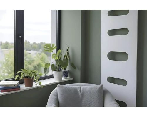 Moderne woonkamer met saliegroene muur, witte designradiator, raam met kamerplanten op de vensterbank en een grijze fauteuil.
