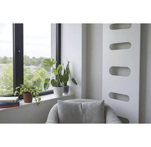 Lichte woonruimte met een moderne radiator, een fauteuil en kamerplanten op de vensterbank naast een raam met een zwart kozijn.