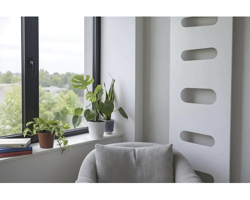 Lichte woonruimte met een moderne radiator, een fauteuil en kamerplanten op de vensterbank naast een raam met een zwart kozijn.