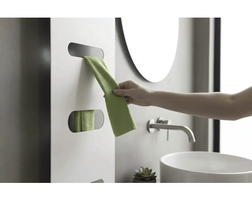 Hand pakt een groene handdoek uit een witte designradiator in een moderne badkamer met wastafel en kraan.