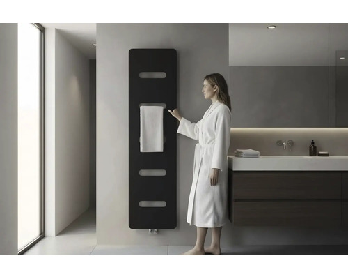 Moderne badkamer met zwarte designradiator aan de wand, een vrouw in een witte badjas en een wastafelmeubel met donkere onderkast.