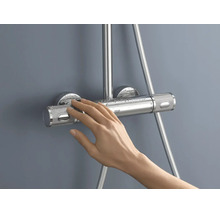 Een hand bedient een chromen Grohe douchethermostaat met getextureerde grepen en waterdruppels.