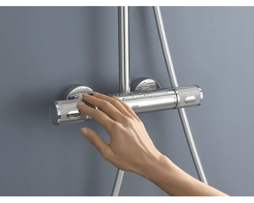 Een hand bedient een chromen Grohe douchethermostaat met getextureerde grepen en waterdruppels.