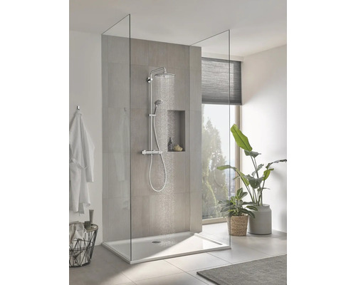 Moderne inloopdouche met glazen wand, chromen regendoucheset en vlakke douchebak in een lichte badkamer met planten.