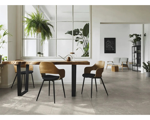 Lichte, moderne kamer met grote vloertegels in steenlook, een houten tafel met boomstamrand en verschillende groene planten.