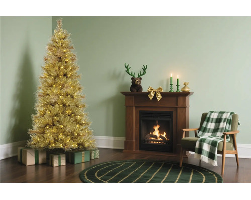 Gouden kerstboom met verlichting naast een houten open haard en een fauteuil met een geruite deken.